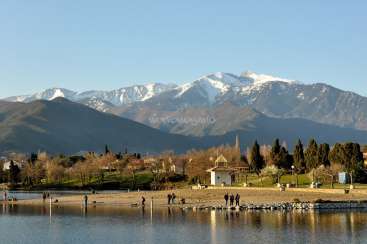 The image depicts a serene lake scene with a majestic mountain range in the background, featuring a sandy beach and lush greenery.