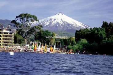 The image depicts a serene lake scene with a majestic snow-capped mountain in the background, surrounded by lush trees and a bustling marina with numerous boats.