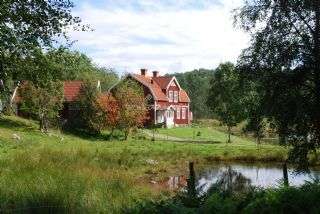 The image depicts a serene rural scene featuring a large house with a red roof, situated beside a tranquil pond and surrounded by lush greenery.