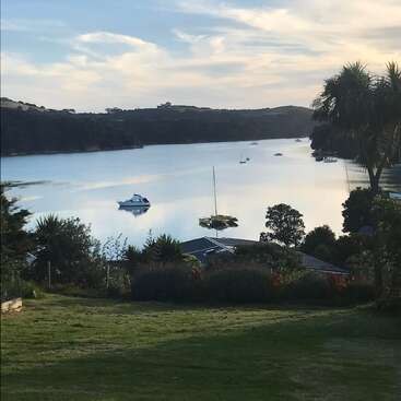 The image depicts a serene lake scene with boats, surrounded by lush greenery and trees, set against a cloudy sky. A house is visible in the foreground.