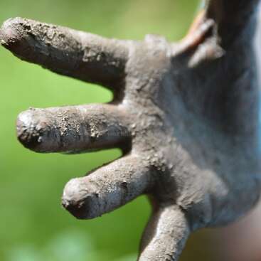 The image depicts a close-up of a hand covered in mud, with the fingers extended and the palm facing downwards, set against a blurred green background.