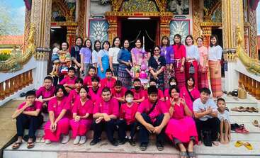The image depicts a group of people gathered in a temple, with a large crowd of individuals standing together, likely for a religious ceremony or event. The scene is peaceful and serene.