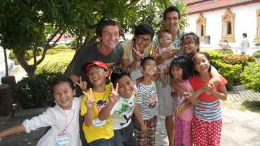 The image depicts a group of children and adults posing for a photo, with the children making peace signs and the adults smiling.